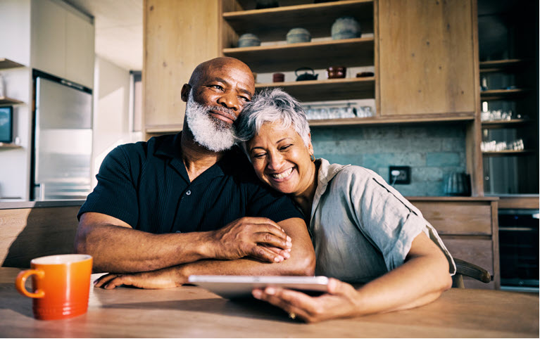 A couple sitting at their kitchen table smiling after reviewing their finances for retirement.