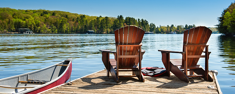 Image of two empty chairs placed on a dock by a lake.