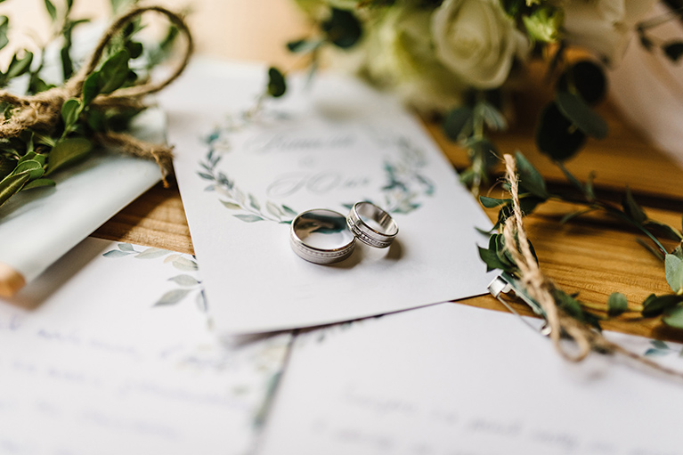 a pair of wedding rings sit atop of wedding invitation and calendar